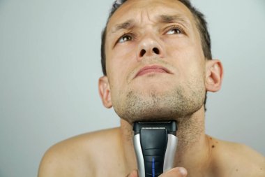Koyu saçlı, güzel bir adam elektrikli jiletle tıraş olur ve kameraya surat yapar..