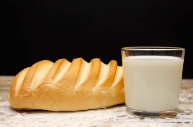 Bir bardak süt ve ahşap bir zemin üzerinde küçük bir somun un ile siyah bir zemin üzerinde uzayın bir kopyası.