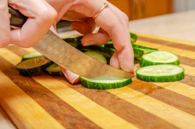 Kadın eli, ahşap bir tabakta salatalıkları yakın mesafeden bıçakla keser.