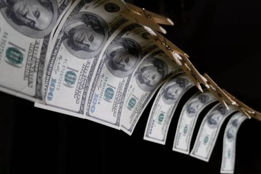 Yüz dolarlık banknotlar siyah arka planda bir ipte mandallarla asılıdır. Kirli para kavramı. Dolar düşüyor..