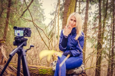 Mavi ceketli ve kot pantolonlu sarışın bir kız, çizmeleri bir blog yazıyor, sanki bir blogcu ormanda oturmuş, devrilmiş bir ağaçta oturuyor, gülümsüyor, kameraya öpücük yolluyor gibi.. DSLR üzerine bir günlük yazar.