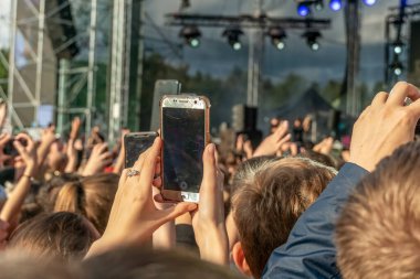 İnsanlar gündüz vakti halk konseri sırasında dokunmatik ekranlı akıllı telefonla fotoğraf çekiyor.