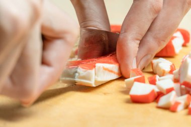 Kadın eli, tahta bir tahtada yengeç sopası keser. Yaklaş.