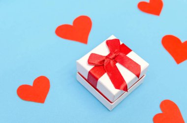 Mavi arka planda kırmızı kağıt kalpler arasında bir hediye kutusu. Üst görünüm, boşluğu kopyala. Sevgililer Günü, aşkın sembolü. Neşeli arkaplan