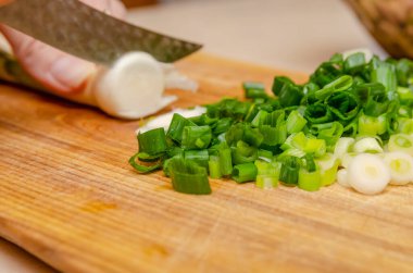 Ahşap bir tahtanın üzerinde yeşil soğanı bıçakla doğrayan kadın eller. sağlıklı beslenme, yemek pişirme, vejetaryen yemekleri