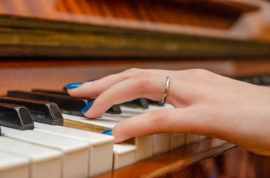 Mavi tırnak cilası olan genç bir kadının eli piyano çalıyor.