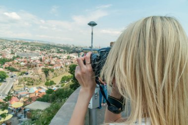Sarışın turist kız güneşli bir günde eski Tiflis şehrini kuş bakışı fotoğraflıyor.
