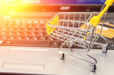 Küçük sarı alışveriş arabası ve kredi kartı olan bir laptop. Online alışveriş kavramı