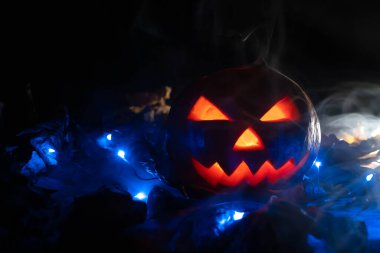 Karanlıkta parlayan balkabağı, mavi ışıklar ve dumanda sonbahar yaprakları. Güzel Cadılar Bayramı arkaplanı, kopyalama alanı.