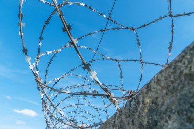 Mavi gökyüzüne karşı çitin etrafına sarılmış dikenli teller.