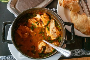 Tahta bir masada, et ve pirinçli Kharcho çorbası ve dökme demir bir kase, yanında da Gürcistan ekmeği var. Yakın çekim fotoğrafı, yukarıdan görünüm