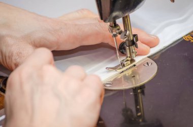 Eski bir dikiş makinesine dikiş diken bir kadının elleri.