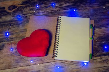 İçinde boş bir kağıt, kırmızı bir kalp ve ahşap bir arka planda mavi bir çelenk olan açık bir defter. Şenlikli, güzel, büyülü, Noel arkaplanı. Üst görünüm, alanı kopyala