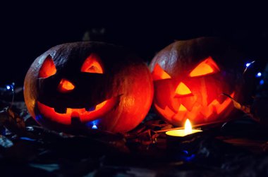 Ormandaki karanlıkta parlayan iki balkabağı, çevrelerinde mumlar. Cadılar Bayramı için güzel bir arkaplan.