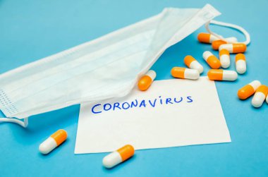 Tıbbi maske, mavi arka planda turuncu-beyaz kapsüller ve beyaz bir sayfada Coronavirus yazılıydı. İlk yardım, hastalık sırasında bakım..