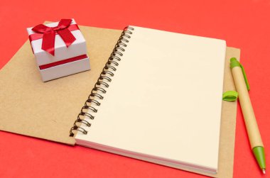 Kırmızı arkaplanda duran kalem ve hediyeli not defteri, boşluğu kopyala.