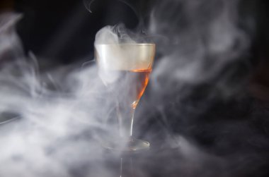 Siyah arka plandaki dumanın içinde bir bardak konyak.