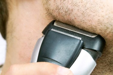 Adam elektrikli jiletle tıraş oluyor.