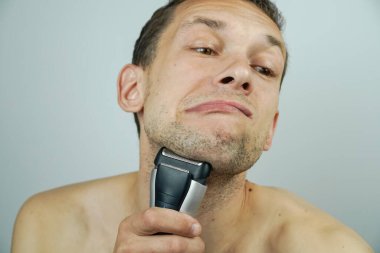 Koyu saçlı, güzel bir adam elektrikli jiletle tıraş olur ve kameraya surat yapar..