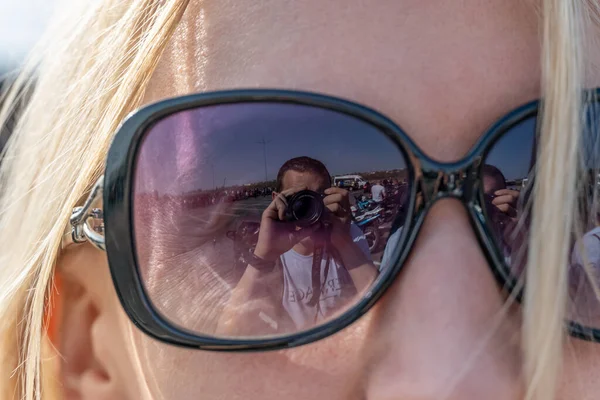 Güneş gözlüklü kız, fotoğrafçının yansıması ve üzerinde kamera var.