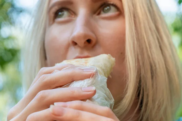 ブロンドの女の子はシャワルマを路上で食べ シャワルマに焦点を当てます ファーストフード ファーストフード — ストック写真