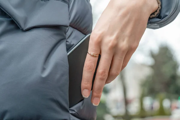 woman\'s hand with a ring pulls a black smartphone out of the pocket of a gray jacket close up