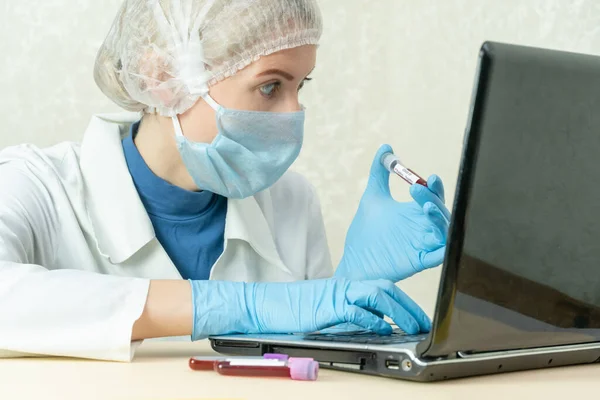 Female doctor in a medical gown, medical mask and cap looks at the laptop with wide-open surprised eyes. Concept of medicine, fear