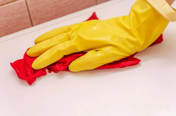 Female hand in a yellow glove with a red rag washes the white surface of the washing machine. The maid cleans the house.