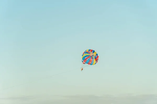 在浅蓝色天空的背景下 带着一个多色降落伞 供寄生人在空中飞行 — 图库照片