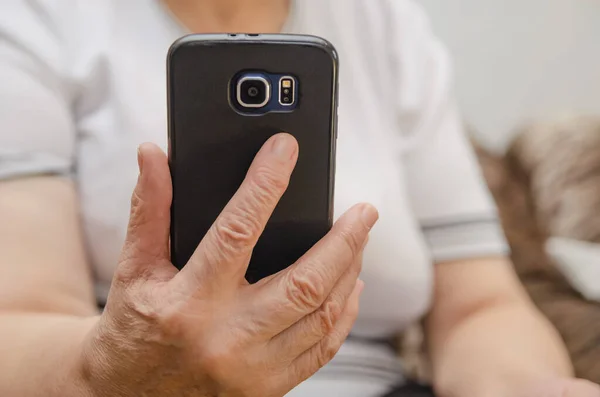 Black mobile phone in the hand of an elderly woman close up