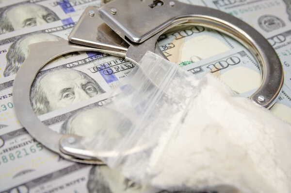 Handcuffs and a bag of drugs close up on dollar bills