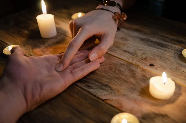 女性占い師は男の手の線を読み取り ろうそくの間で木製の背景に手を自分の将来を予測します 魔法占いという概念は — ストック写真