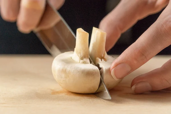 woman\'s hand with a knife cuts a white mushroom close up on a wooden Board
