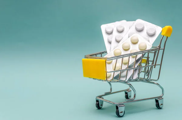 Shopping cart with pills on a blue background close-up. The concept of the medicine of online shopping. Copy space for text