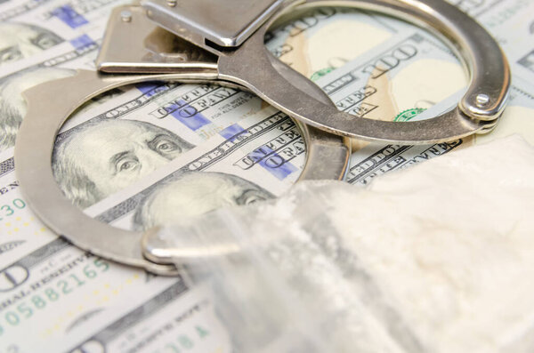 Handcuffs and a bag of drugs close up on dollar bills