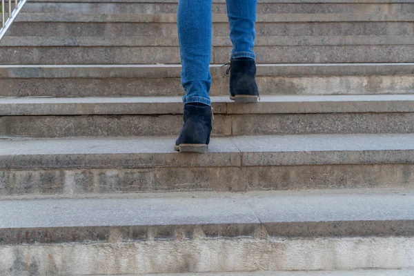 Closeup of legs of a woman in jeans and blue shoes walking upstairs