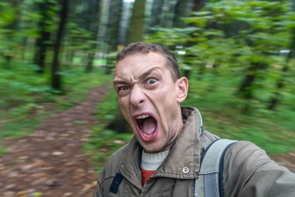 brunette man screaming in the forest in a frightened voice, portrait of a screaming man with his mouth wide open in the autumn forest