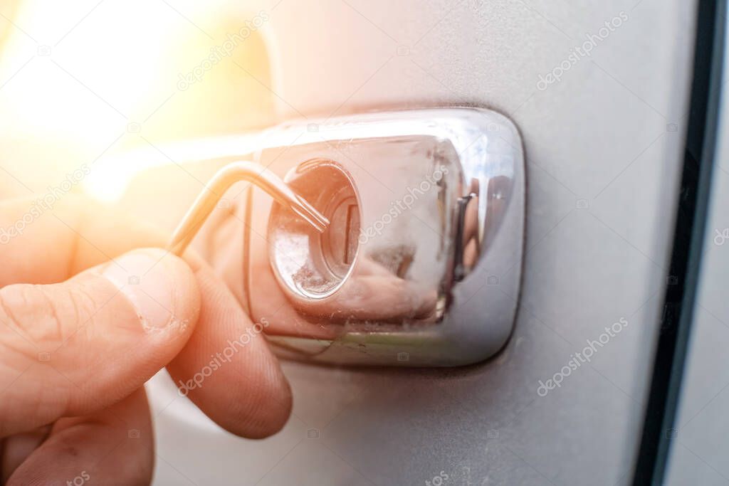 Car thief. Close - up of a man's hands opening the car with a lock pick. Photo with illumination, light