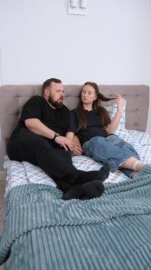 Happy young couple relaxing together in bed, sharing heart-warming conversations and tender moments in a cozy bedroom setting that represents authentic connection and home comfort vertical video