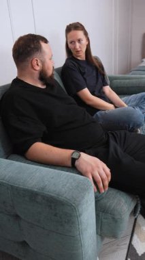 A man and a woman are sitting on a comfortable sofa, having a lively conversation, gesturing to emphasize their points of view in the cozy atmosphere of the living room. vertical video