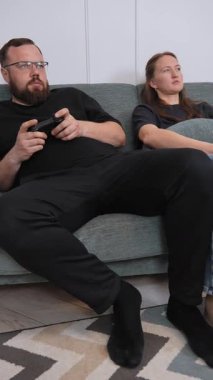 Relaxing young couple spending quality time together, lounging on comfortable sofa while sharing popcorn and enjoying movie night in cozy living room vertical video