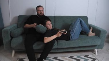 Young couple participating in competitive video games, sitting comfortably on the sofa in the living room, sharing playful moments of technological entertainment and building relationships
