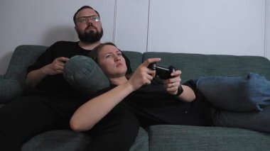 Young couple participating in competitive video games, sitting comfortably on the sofa in the living room, sharing playful moments of technological entertainment and building relationships