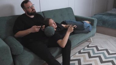 Young couple participating in competitive video games, sitting comfortably on the sofa in the living room, sharing playful moments of technological entertainment and building relationships