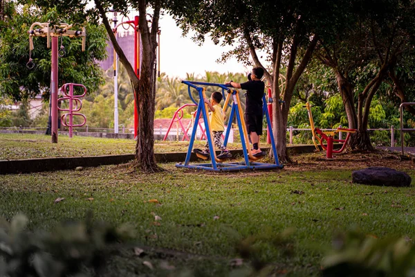 Alacakaranlıkta bir oyun alanında oynayan iki kardeş..