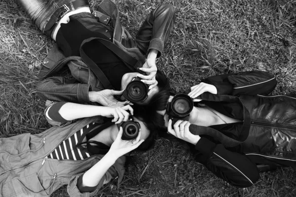 三个年轻的女孩躺在草地上 手里拿着摄像机 眼睛盯着镜头 心情好 黑白相间 公园里的户外摄影记者 — 图库照片