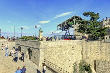 San Marino, San Marino - 19 Ekim 2019: Renkli çiçekler ve turistler ön planda ve arka planda teleferik mekanizmasında izleme platformu boyunca manzara.