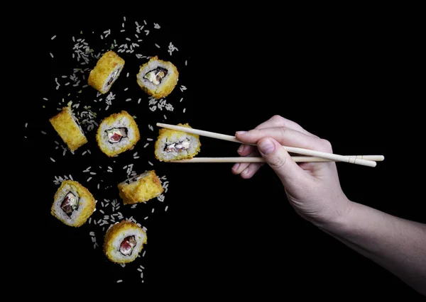 Latające Żółte Sushi Tempura Ryżem Czarnym Tle Ich Ręka Łapie — Zdjęcie stockowe