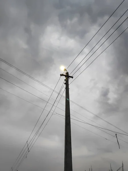 Bulutlu havada ampullü lamba direği ve yanında ve üstünde elektrik kabloları var.