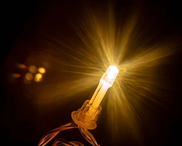 Karanlığı parlak hacimli aydınlatmalarla aydınlatan tek bir Noel ışığı. Siyah Arkaplan.